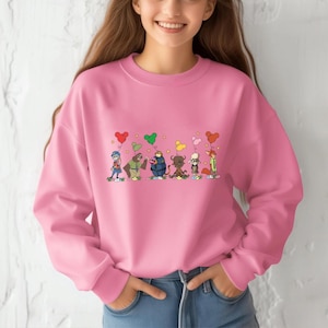 A woman wearing a pink sweatshirt with a graphic of cartoon characters and hearts on it.