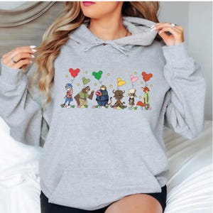 A woman wearing a gray hoodie with a graphic design of cartoon characters and hearts on it.