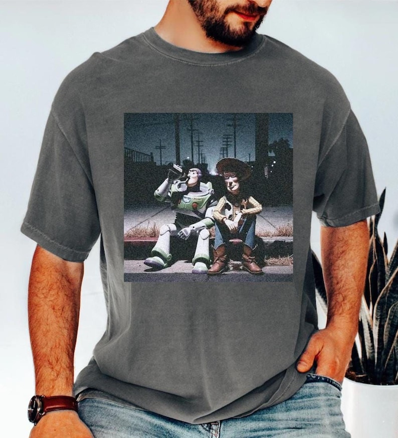 A man wearing a gray t-shirt with a graphic of two people sitting on a bench.
