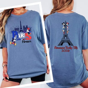 A woman wearing a blue t-shirt with a graphic of Paris and Mickey Mouse, along with the text "Paris" and "Amber". The t-shirt also features a graphic of the Eiffel Tower and the text "Anderson Family Trip 2016".