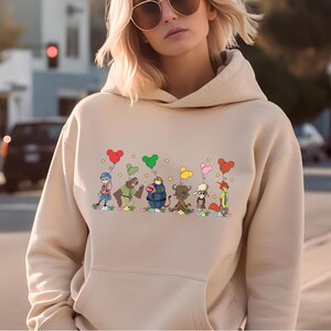 A woman wearing a beige hoodie with a graphic of cartoon characters and balloons on it.