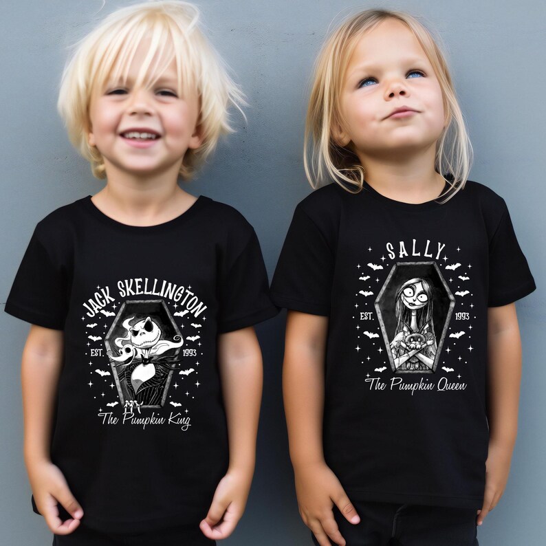 Pu&ograve; includere: Due bambini indossano magliette nere con grafiche bianche. Una maglietta dice "Jack Skellington" con un disegno a bara e "The Pumpkin King". L'altra dice "Sally" con un disegno a bara e "The Pumpkin Queen". Entrambe le magliette hanno "EST. 1993."
