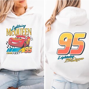 Puede incluir: Sudadera con capucha blanca con gr&aacute;ficos de Lightning McQueen. La parte delantera muestra un coche de carreras rojo con el texto "Lightning McQueen" y "95". La parte trasera tiene un gran gr&aacute;fico "95" y el texto "Lightning McQueen".