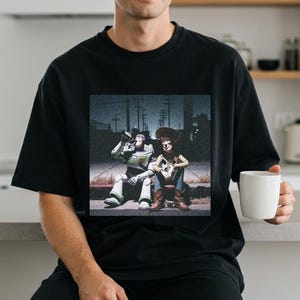A person wearing a black t-shirt with a graphic of two characters from the Toy Story franchise, Buzz Lightyear and Woody, sitting together.