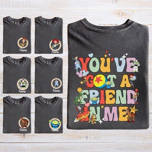 A collection of gray t-shirts with various cartoon character designs and text, along with a t-shirt featuring a colorful, playful design with the text "You've Got a Friend in Me".