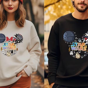 Pu&ograve; includere: Due felpe con un design a testa di Topolino con personaggi di Star Wars e il testo "Star Wars". La felpa a sinistra &egrave; beige e la felpa a destra &egrave; nera.