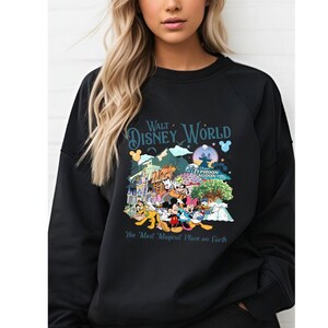 A woman wearing a black sweatshirt with a colorful graphic design featuring Disney characters and landmarks.