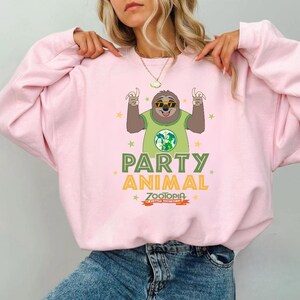 A woman wearing a pink sweatshirt with a cartoon sloth character and the text "Party Animal" printed on it.