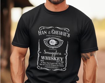 May include: Black t-shirt with a white graphic of a whiskey label that says "Han & Chewie's Twelve Parsec Straight Smugglers Whiskey 70cl 45% Vol. It May Not Look Like Much But It's Got It Where It Counts Distilled and Bottled by Tatogene Distillery"