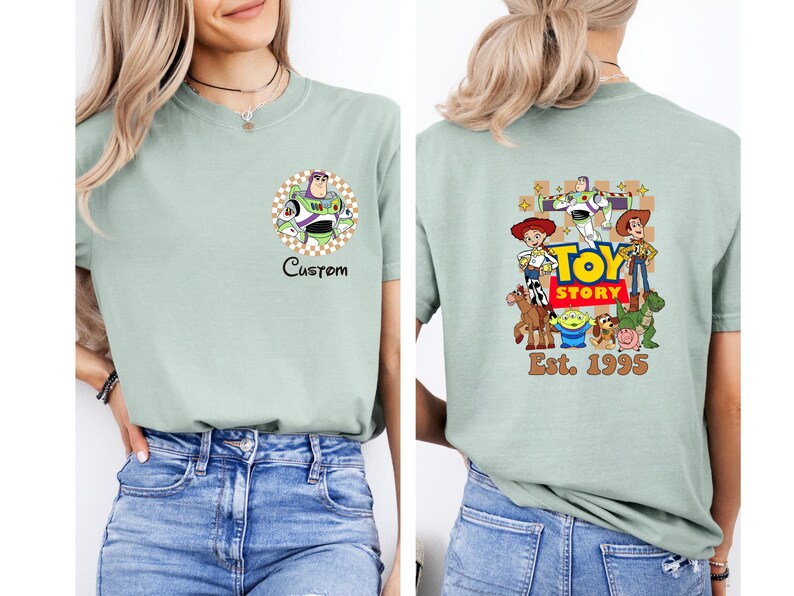 Puede incluir: Camiseta verde claro con un gr&aacute;fico de Buzz Lightyear en la parte delantera y un gr&aacute;fico de Toy Story en la parte trasera. El gr&aacute;fico frontal incluye la palabra "Custom". El gr&aacute;fico trasero incluye el texto "Toy Story" y "Est. 1995".