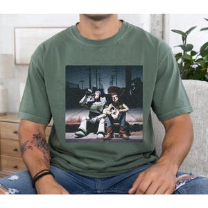 A person wearing a green t-shirt with a printed image of two people sitting on a bench.