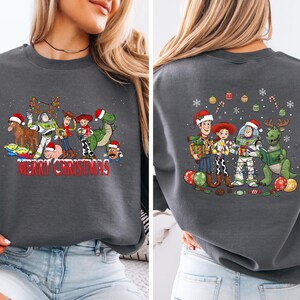 May include: Dark gray sweatshirt featuring a festive graphic of animated characters in Santa hats and Christmas lights. The front of the sweatshirt reads "Merry Christmas" in red. The back of the sweatshirt also features the same characters.