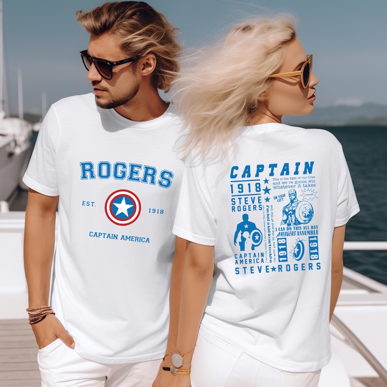 Puede incluir: Dos camisetas blancas con tem&aacute;tica de Capit&aacute;n Am&eacute;rica. La parte delantera de la camiseta tiene el texto "ROGERS" con un escudo de Capit&aacute;n Am&eacute;rica rojo, blanco y azul y el texto "EST. 1918" y "CAPTAIN AMERICA". La parte trasera de la camiseta tiene el texto "CAPTAIN 1918 STEVE ROGERS" con un escudo de Capit&aacute;n Am&eacute;rica y el texto "I CAN DO THIS ALL DAY" y "AVENGERS ASSEMBLE 1918 1918 STEVE ROGERS".