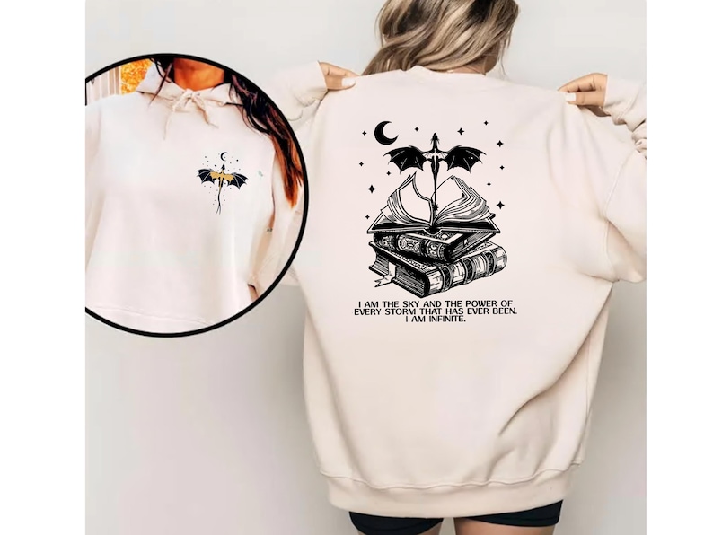 A person wearing a white sweatshirt with a black graphic design on the back, which features a dragon, books, and a crescent moon.