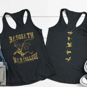 a pair of black tank tops with gold text and graphics, laid out on a white surface alongside some jeans, sneakers, and a potted plant.
