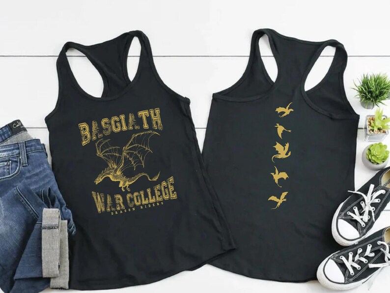a pair of black tank tops with gold text and graphics, laid out on a white surface alongside some jeans, sneakers, and a potted plant.