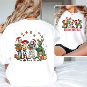 May include: White sweatshirt featuring a colorful graphic of Toy Story characters in Santa hats and Christmas decorations. The front of the sweatshirt has the text "MERRY CHRISTMAS". The back of the sweatshirt has the same characters and decorations.