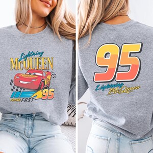 Puede incluir: Sudadera gris con Lightning McQueen de la pel&iacute;cula Cars. La parte delantera muestra el personaje y los textos "Lightning McQueen" y "Think Fast". La parte trasera tiene un gran gr&aacute;fico "95" y el texto "Lightning McQueen".