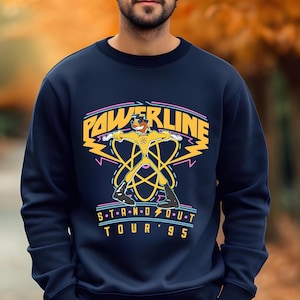 May include: A navy blue sweatshirt with a yellow cartoon character in a superhero pose. The text "POWERLINE STAND OUT TOUR '95" is printed on the front of the sweatshirt.