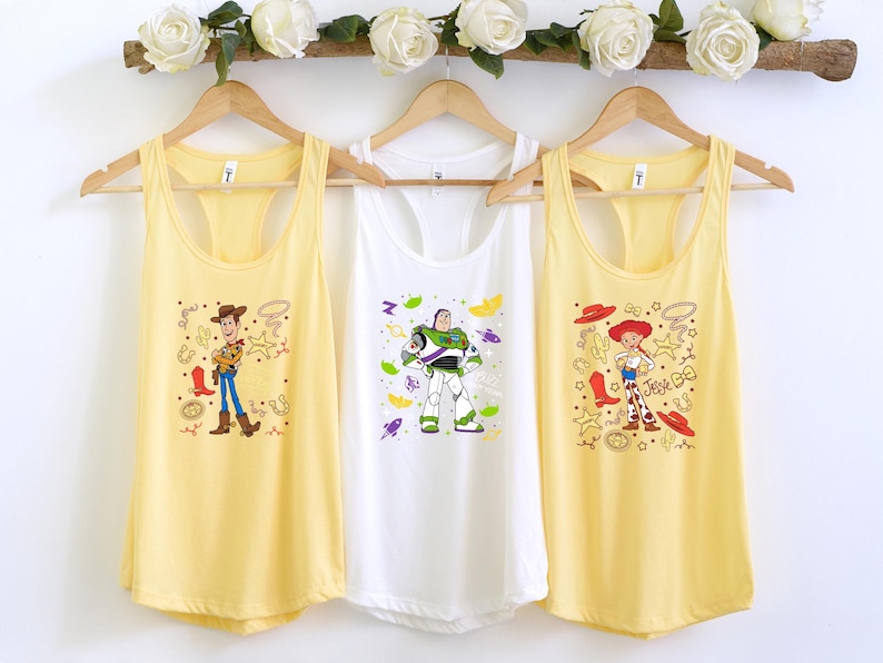 Three yellow tank tops hanging on a wooden hanger, each featuring a different character from the Toy Story franchise.