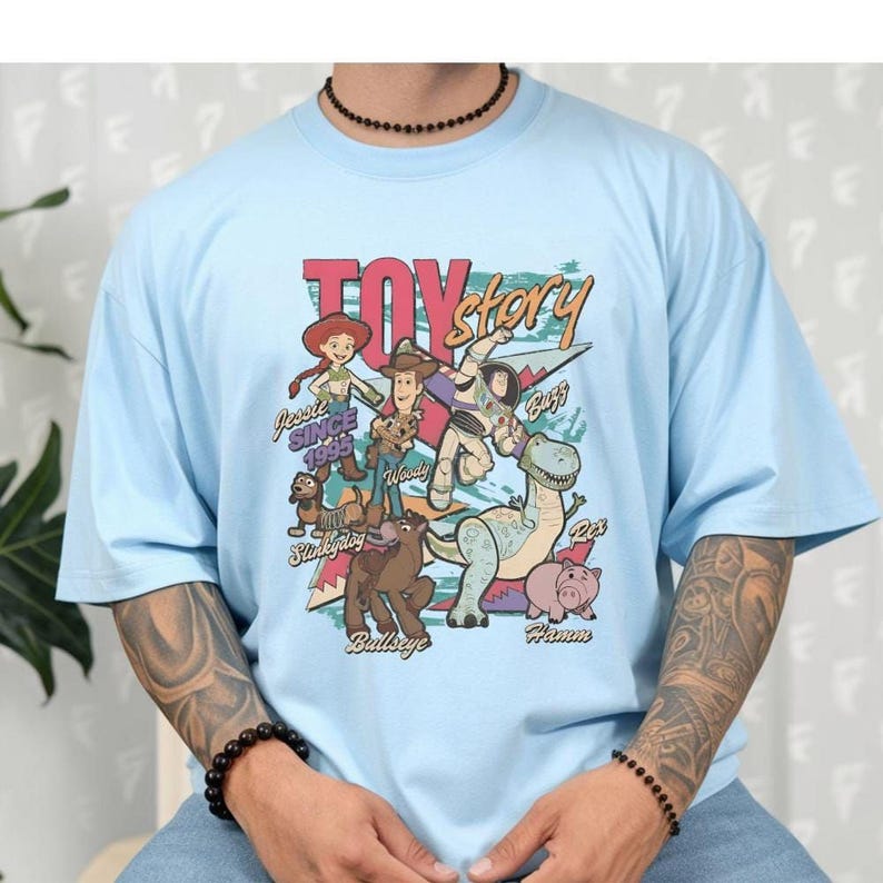 A person wearing a light blue t-shirt with a colorful graphic design featuring characters from the Toy Story movie.