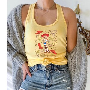 A person wearing a yellow tank top with a cartoon character printed on it, paired with denim shorts and a gray cardigan.