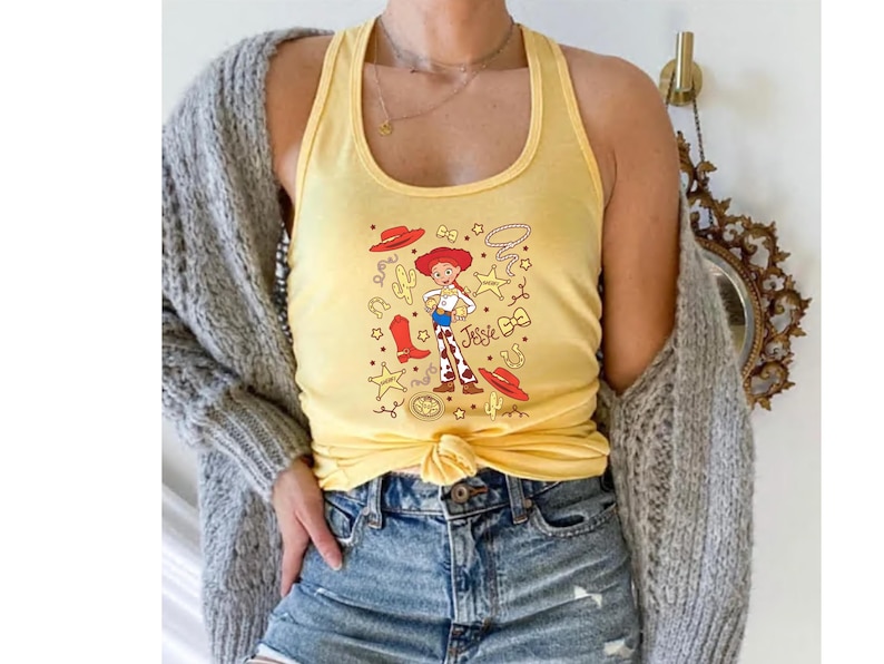 A person wearing a yellow tank top with a cartoon character printed on it, paired with denim shorts and a gray cardigan.