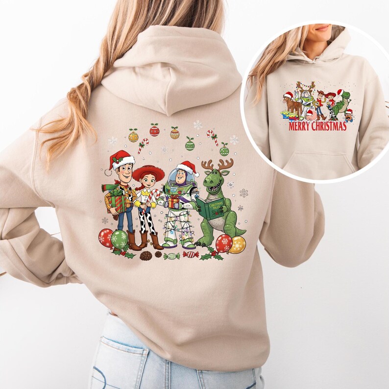 May include: Beige hoodie featuring a colorful graphic of animated characters in Santa hats, holding gifts and reading a book. The design includes Christmas ornaments and candy canes. The smaller image on the right says "MERRY CHRISTMAS" in red.