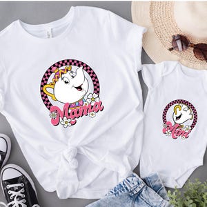 May include: White t-shirts and a onesie featuring a cartoon teapot design with the words "Mama" and "Mom" in pink script. The design is set within a pink and black checkered circle, with floral accents. Black sneakers are visible.