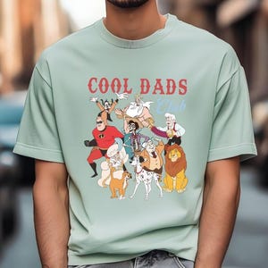 A man wearing a light green t-shirt with a graphic design featuring various cartoon characters.