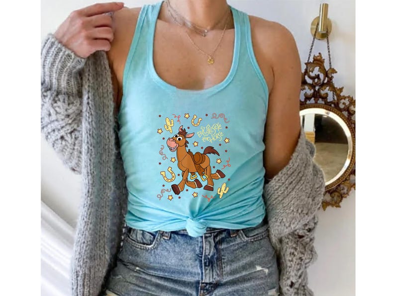 A woman wearing a turquoise tank top with a cartoon horse design and a gray cardigan.