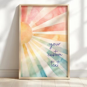 May include: A framed watercolor print featuring a sunburst design in shades of pink, orange, yellow, green, and blue. The text "your custom text" is written in a cursive font. The artwork is displayed in a light-colored wooden frame.