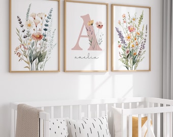 May include: Three framed floral art prints with a light wood finish. The prints feature watercolor illustrations of wildflowers and the letter "A" with the name "amelia" in script. The color palette includes pinks, greens, and yellows.
