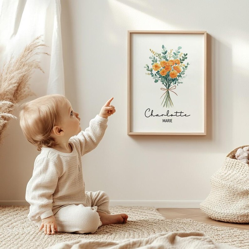 May include: A framed floral print featuring a watercolor bouquet of orange flowers and green foliage, tied with a brown ribbon. The print includes the name "Charlotte" and "MARIE" in script. A child points at the artwork.