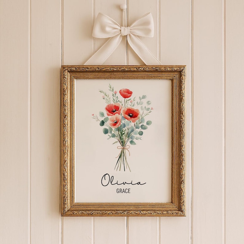 Puede incluir: Una impresi&oacute;n floral enmarcada con un ramo de acuarela de amapolas rojas y follaje verde, atado con hilo. La impresi&oacute;n est&aacute; en un marco dorado adornado y est&aacute; suspendida por un lazo color crema. Los nombres "Olivia" y "Grace" est&aacute;n escritos en cursiva.