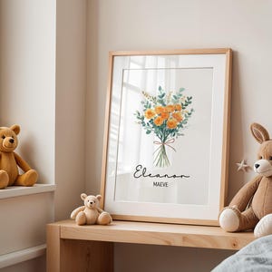 May include: A framed floral print featuring a watercolor bouquet of orange flowers and green foliage tied with a red ribbon. The print includes the names "Eleanor" and "Maeve" in elegant script. The frame is light wood.
