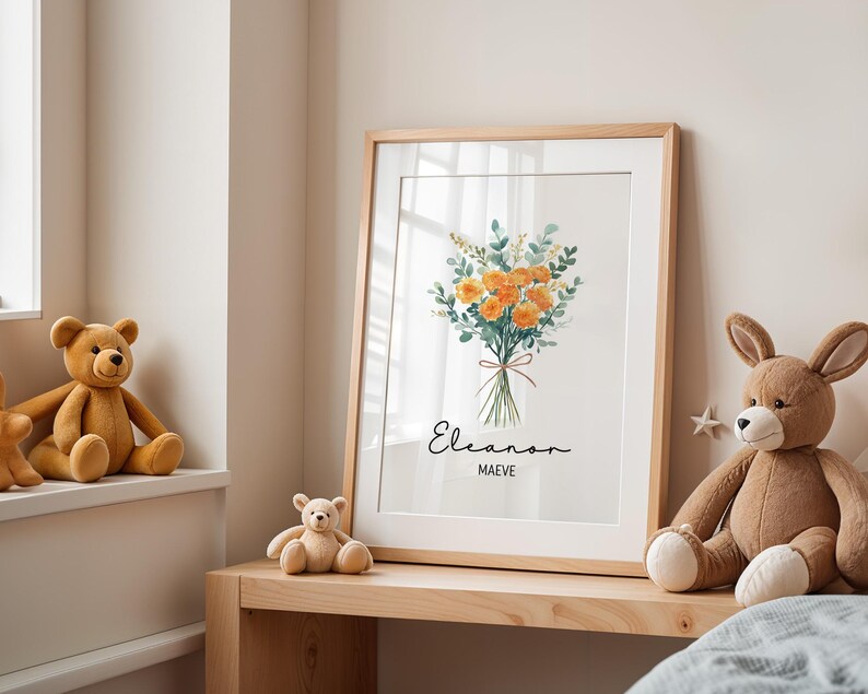 May include: A framed floral print featuring a watercolor bouquet of orange flowers and green foliage tied with a red ribbon. The print includes the names "Eleanor" and "Maeve" in elegant script. The frame is light wood.