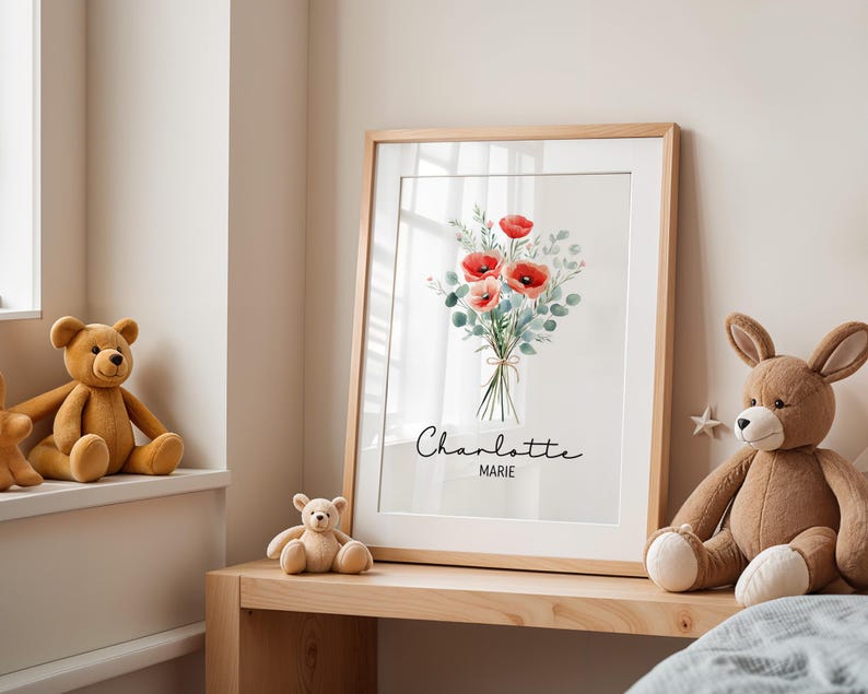 Puede incluir: Una impresi&oacute;n art&iacute;stica enmarcada con un ramo de acuarela de amapolas rojas y follaje verde, atado con hilo. La impresi&oacute;n est&aacute; en un marco de madera clara e incluye los nombres "Charlotte Marie". La obra de arte se exhibe en una estanter&iacute;a de madera.