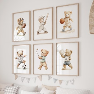 May include: Six framed watercolour prints depicting teddy bears engaged in various sports: American football, baseball, basketball, football (soccer), golf, and volleyball. Each bear is dressed in sports attire and holds equipment. The frames are light wood.