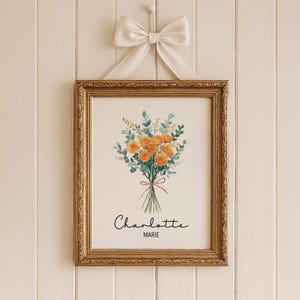 May include: A framed floral print featuring a bouquet of orange flowers and green foliage tied with a brown ribbon. The print is in a gold ornate frame and is hanging from a white bow. The name "Charlotte Marie" is written in script below the flowers.