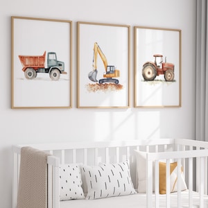 May include: Set of three framed watercolor prints featuring construction vehicles. The prints depict a dump truck, excavator, and tractor in shades of orange, yellow, and green. The artwork is set against a white background, framed in light wood, and suitable for a nursery.