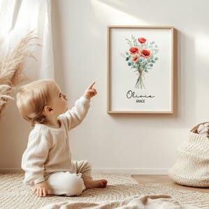 Puede incluir: Una impresi&oacute;n art&iacute;stica floral enmarcada con un ramo de acuarela de amapolas rojas y follaje verde, atado con hilo. La impresi&oacute;n incluye los nombres "Olivia" y "Grace" en una elegante escritura. La obra de arte se exhibe en una pared clara.