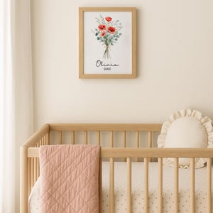 Puede incluir: Un cuadro con una impresi&oacute;n floral de amapolas rojas y follaje verde, con el nombre "Olivia" y la palabra "Grace" debajo. El cuadro cuelga sobre una cuna de madera con una manta acolchada rosa y una almohada color crema.