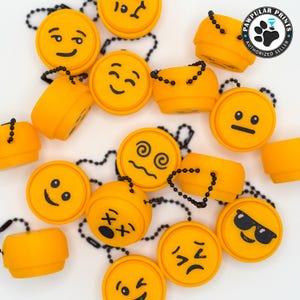 May include: A collection of 14 yellow rubber keychains with different emoji faces. Each keychain has a black chain attached. The keychains are arranged on a white surface. The text "PAWPULAR PRINTS AUTHORIZED SELLER" is visible in the top right corner of the image.