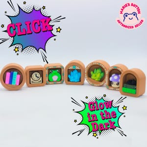 Könnte beinhalten: Eine Reihe brauner dekorativer Knöpfe mit verschiedenen Designs, darunter Bücher, eine Uhr, ein Frosch, blaue Kristalle, grüne Pflanzen, ein Pilz und ein Stapel Bücher. Die Knöpfe sind in einer Reihe angeordnet. Der Text "CLICK" und "Glow in the Dark" sind ebenfalls sichtbar.