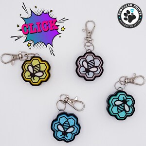 Può includere: Quattro portachiavi con un designo di ape in un alveare. I portachiavi sono in giallo, rosa, blu e nero. Ogni portachiavi ha un anello di metallo argentato e una chiusura di metallo argentato.