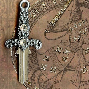 Puede incluir: Una llave decorativa con diseño de espada, con un mango de metal plateado adornado con gemas transparentes. La llave se encuentra sobre una ilustración de estilo vintage de un caballero, con detalles de purpurina dorada.
