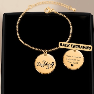 May include: A gold-colored bracelet with two circular pendants and a rectangular tag. One pendant says "Daddy's" in script, the other says "Your custom message on the back" with a heart. The tag reads "BACK ENGRAVING".