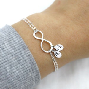 May include: Silver infinity bracelet with two small charms, each with a letter, E and N, hanging from it.