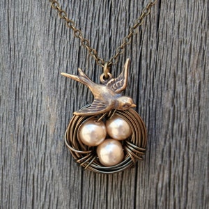 May include: A gold necklace with a bird and nest pendant. The nest is made of wire and contains three pearl-like beads.